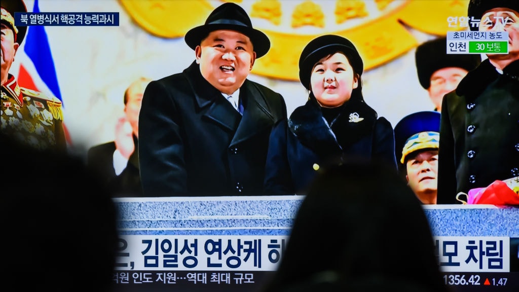 People watch a television screen showing a news broadcast with an image of North Korean leader Kim Jong-un (L) and his daughter presumed to be named Ju-ae (R) attending a military parade held in Pyongyang to mark the 75th founding anniversary of its armed forces, at Yongsan railway station in Seoul.