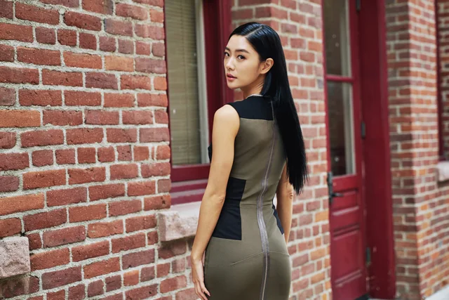 Clara Lee looking back over her shoulder beside a brick wall