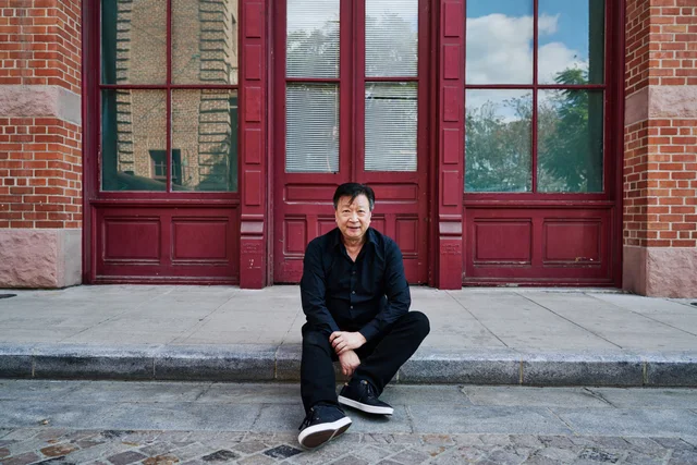 Tzi Ma seated outside red doors