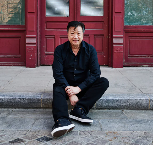 Tzi Ma seated outside red doors